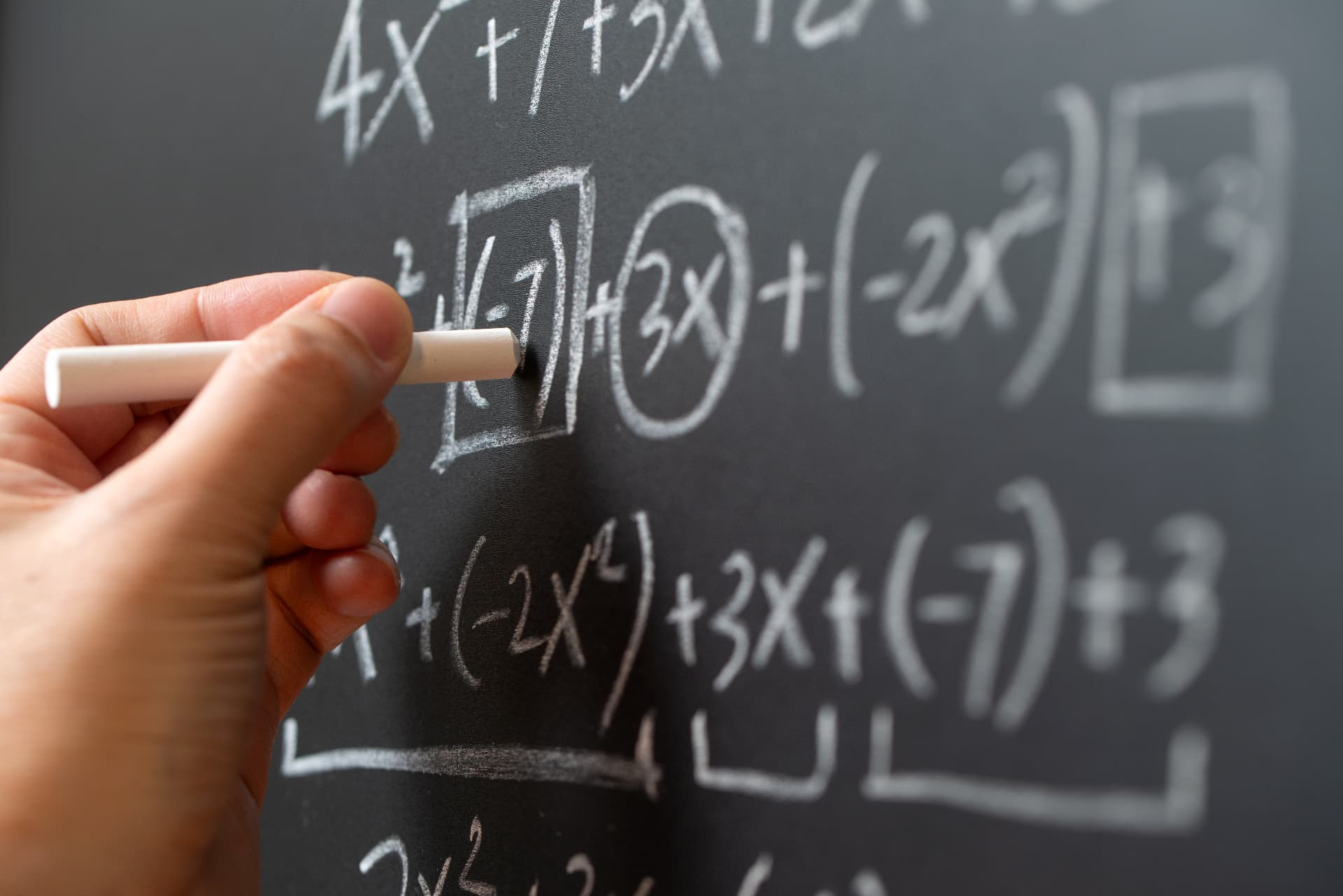A hand writing an equation on a chalkboard